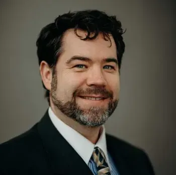 A man with a beard wearing a suit and tie is smiling for the camera.