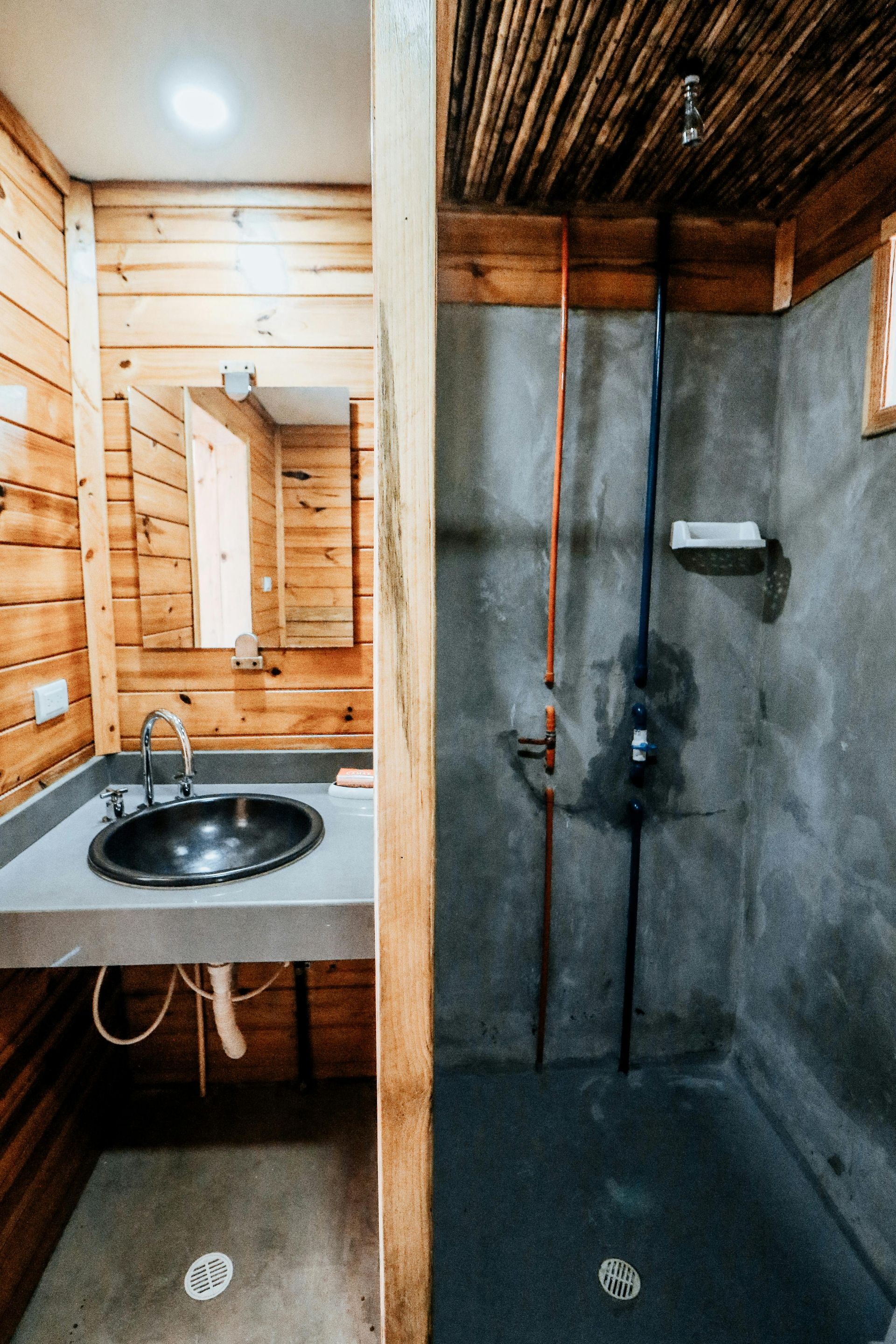 Bathroom with wooden walls, concrete shower, and sink area with a mirror.