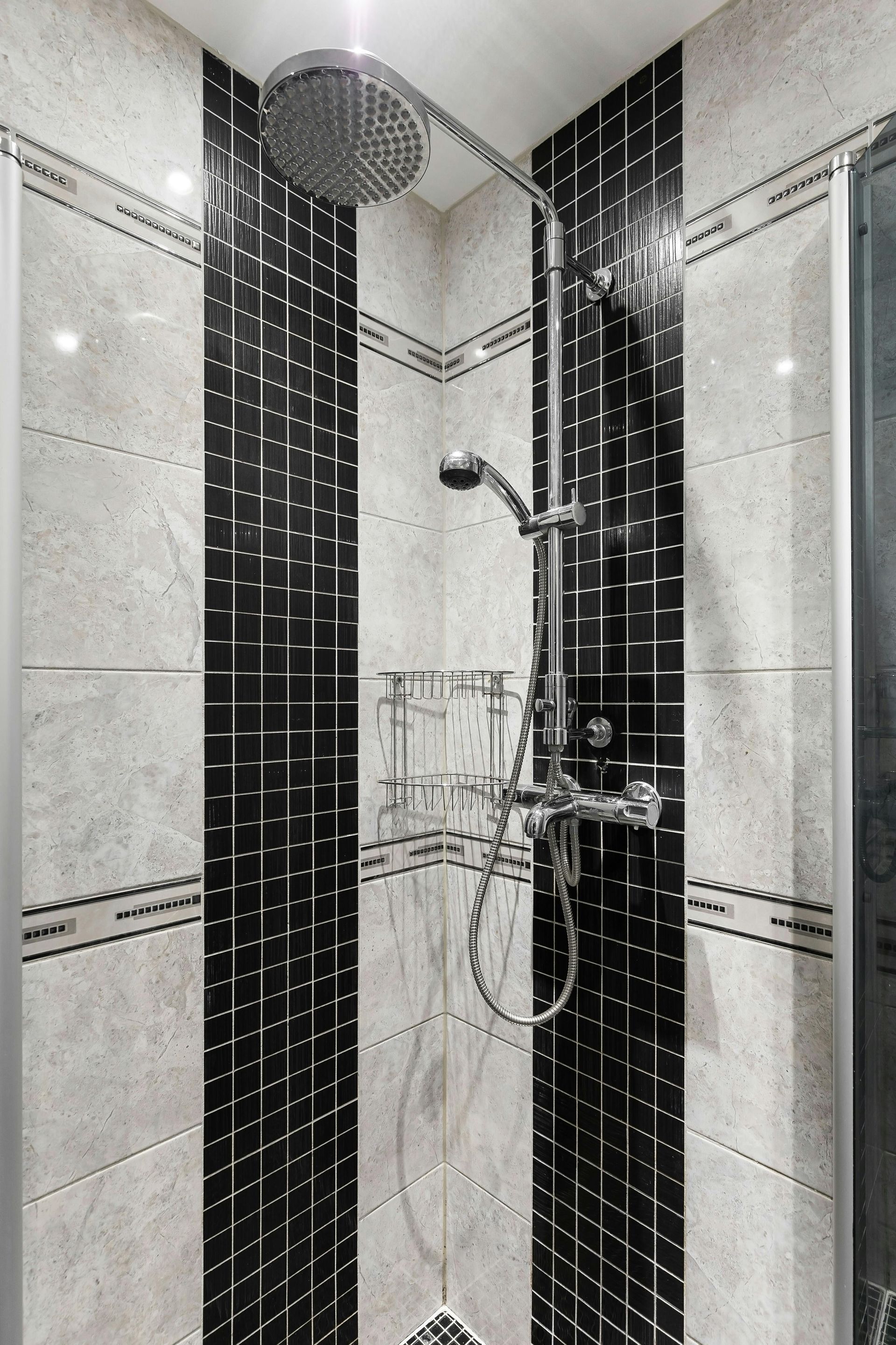 Shower with black and white tiled walls, a large overhead showerhead, and a hand shower.