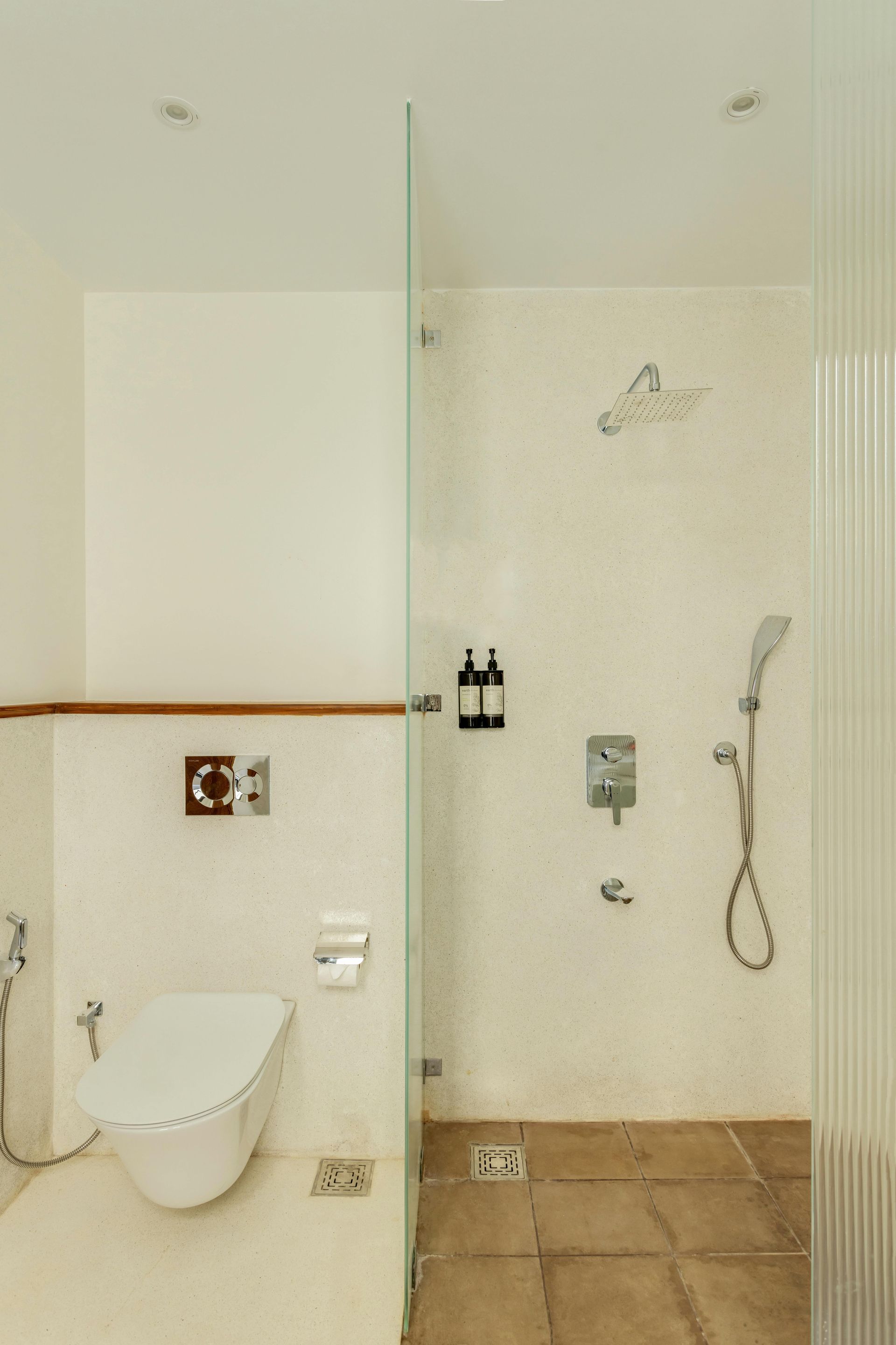 Modern bathroom with a toilet, shower, and glass enclosure. Beige walls and stone tile floors.