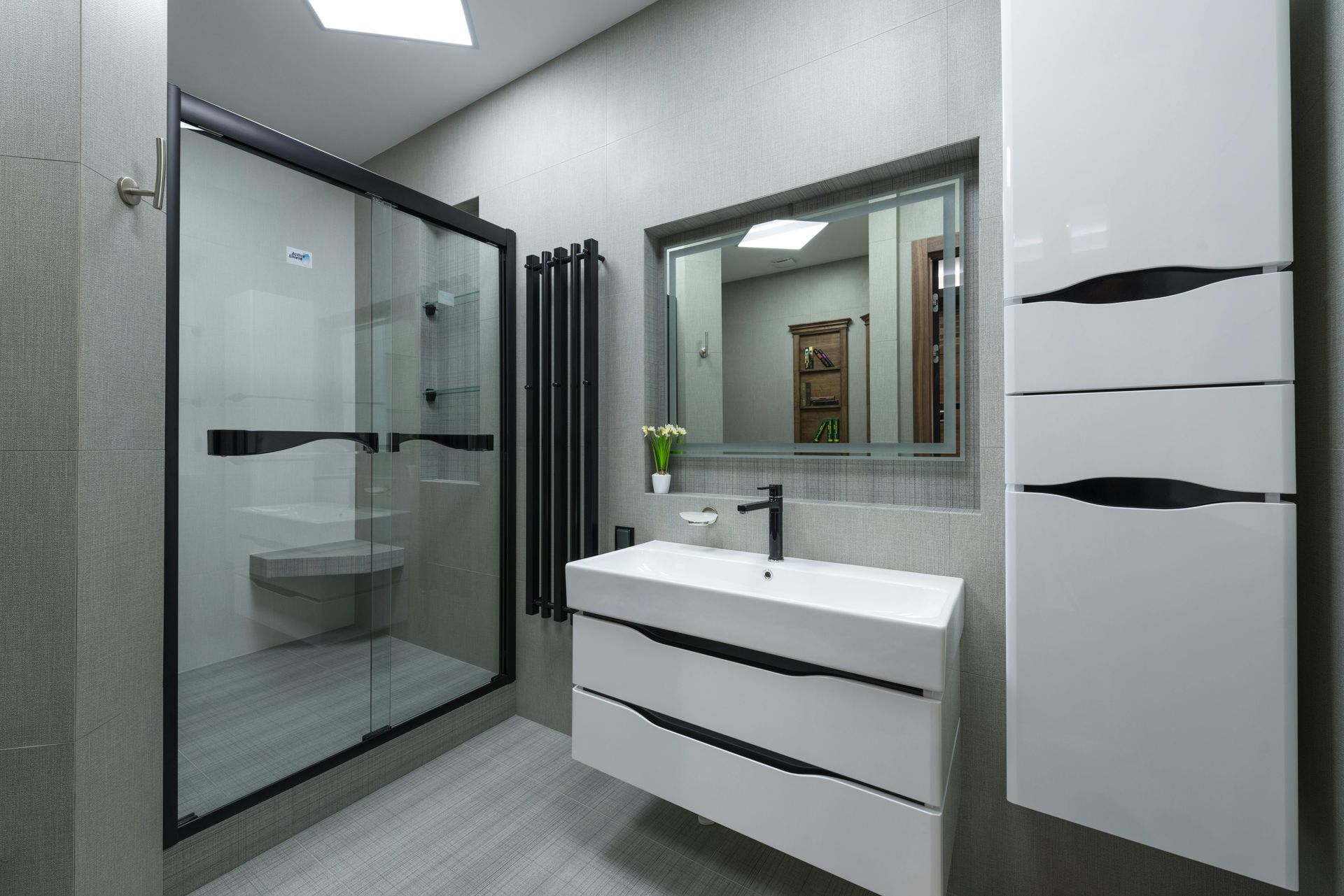 Modern bathroom with glass shower, white vanity, mirror, and tall white cabinet.