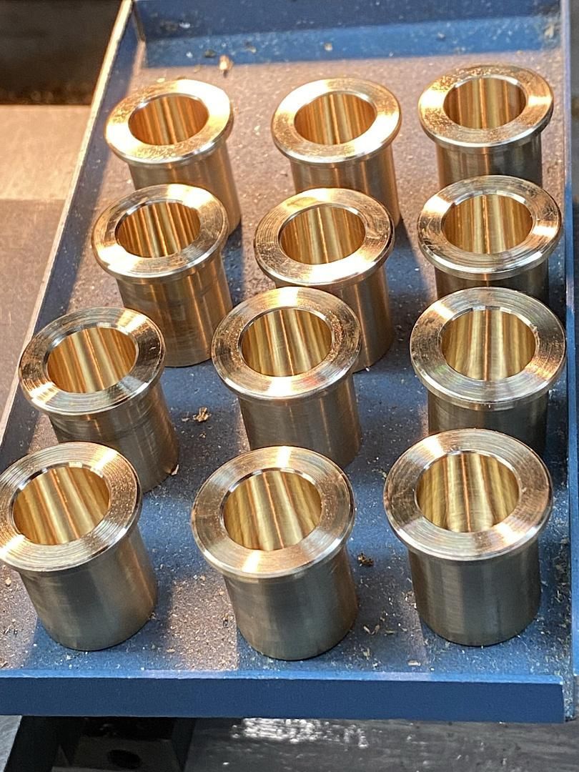 A tray of brass bushings with holes in them on a table.