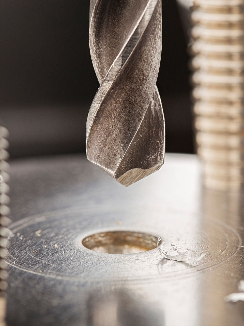 A close up of a drill bit cutting a hole in a metal object.