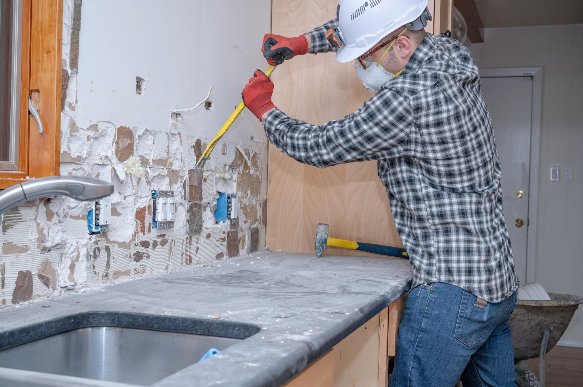 A man is working on a kitchen counter with a tape measure and a hammer.