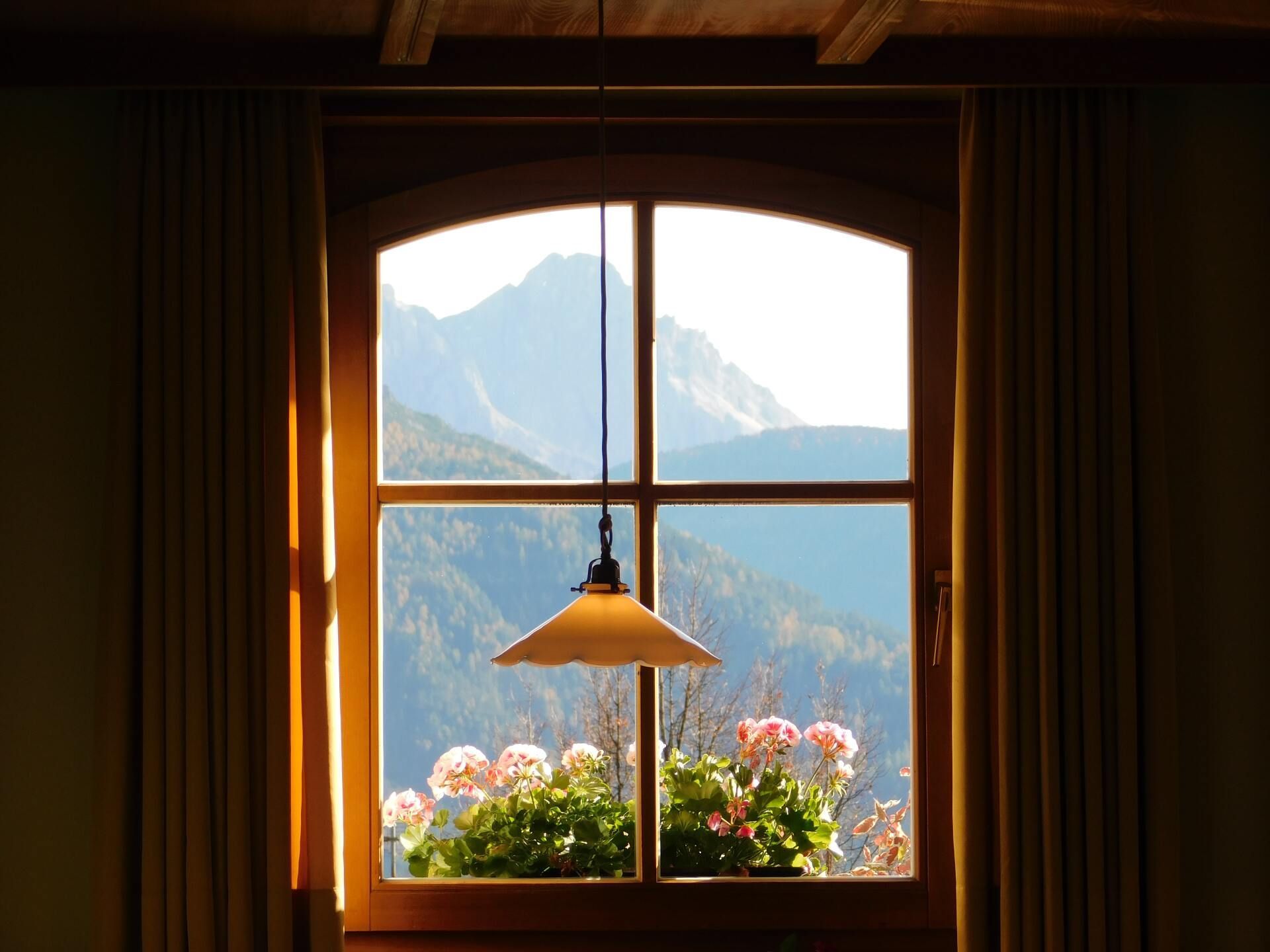 Cozy wooden room window framing mountain view, hanging lamp, and flower box in warm sunlight