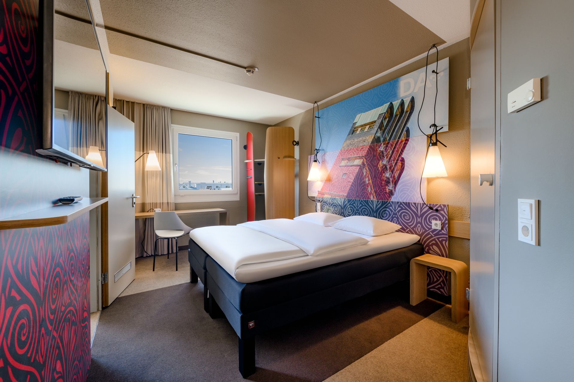 Modernes Hotelzimmer mit Bett, Schreibtisch, Fenster und farbenfroher Wandkunst