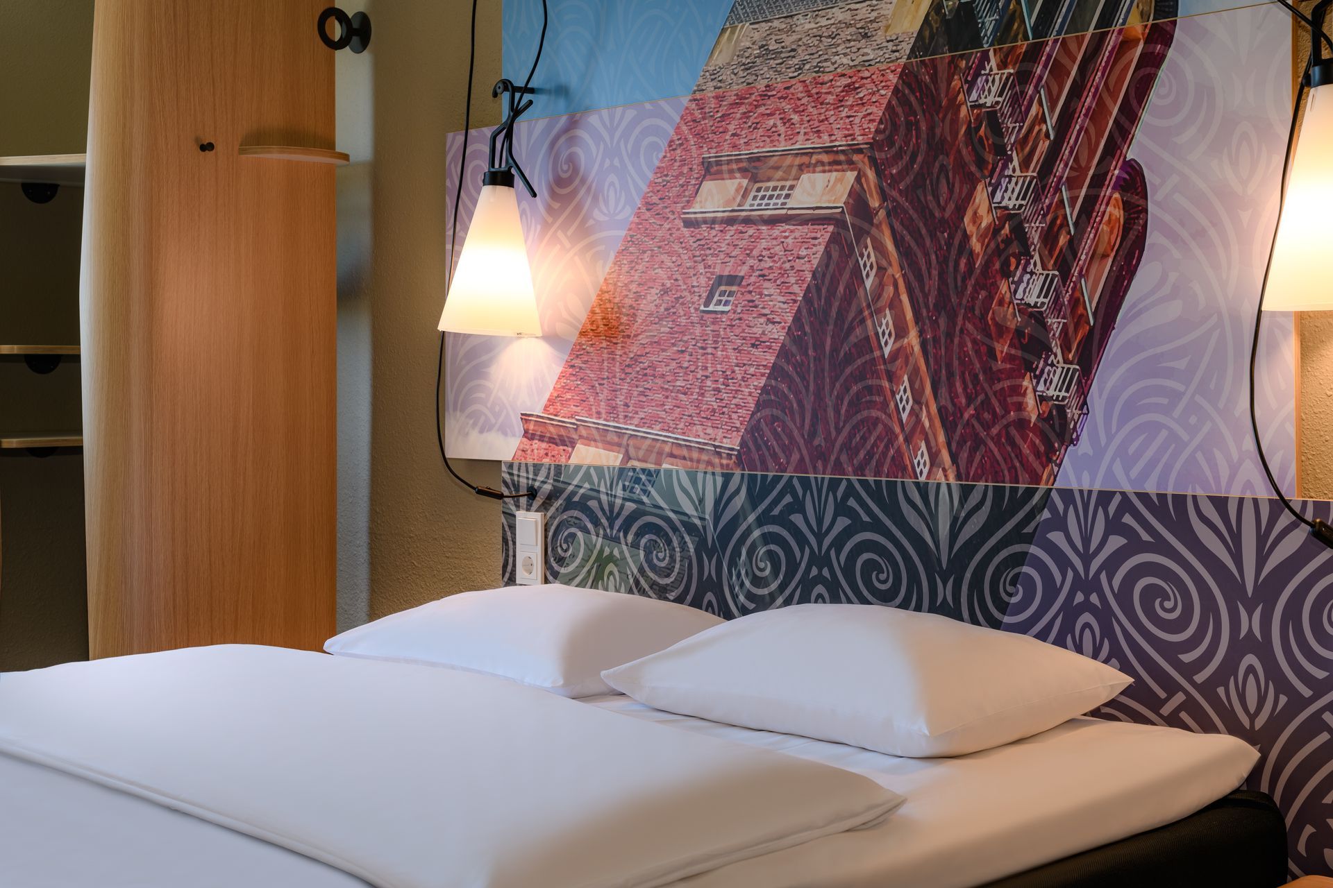 Modern bedroom with white bed, hanging lamp, and colorful geometric wall mural