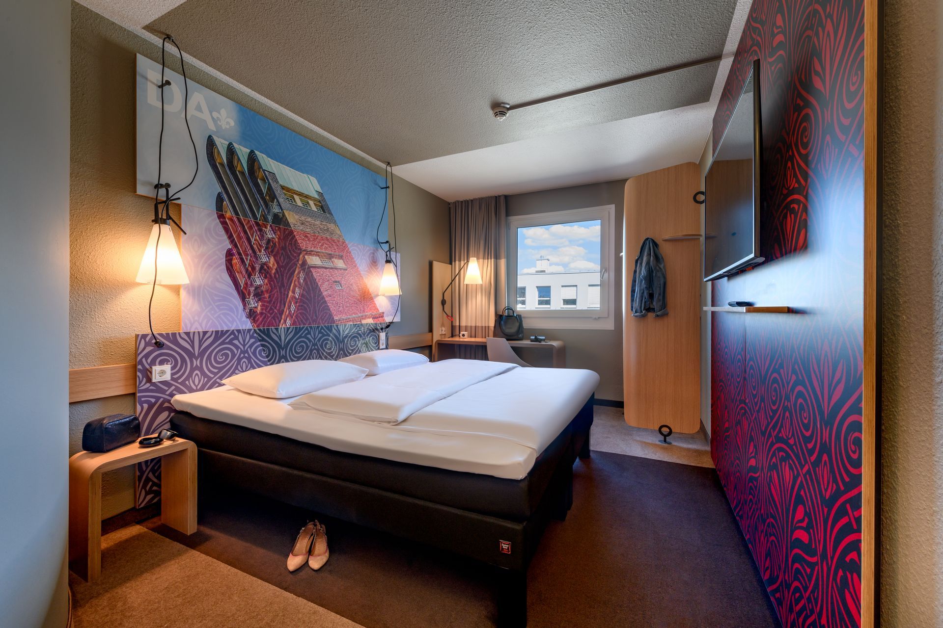 Modern hotel room with a neatly made bed, warm lamps, and colorful wall art.