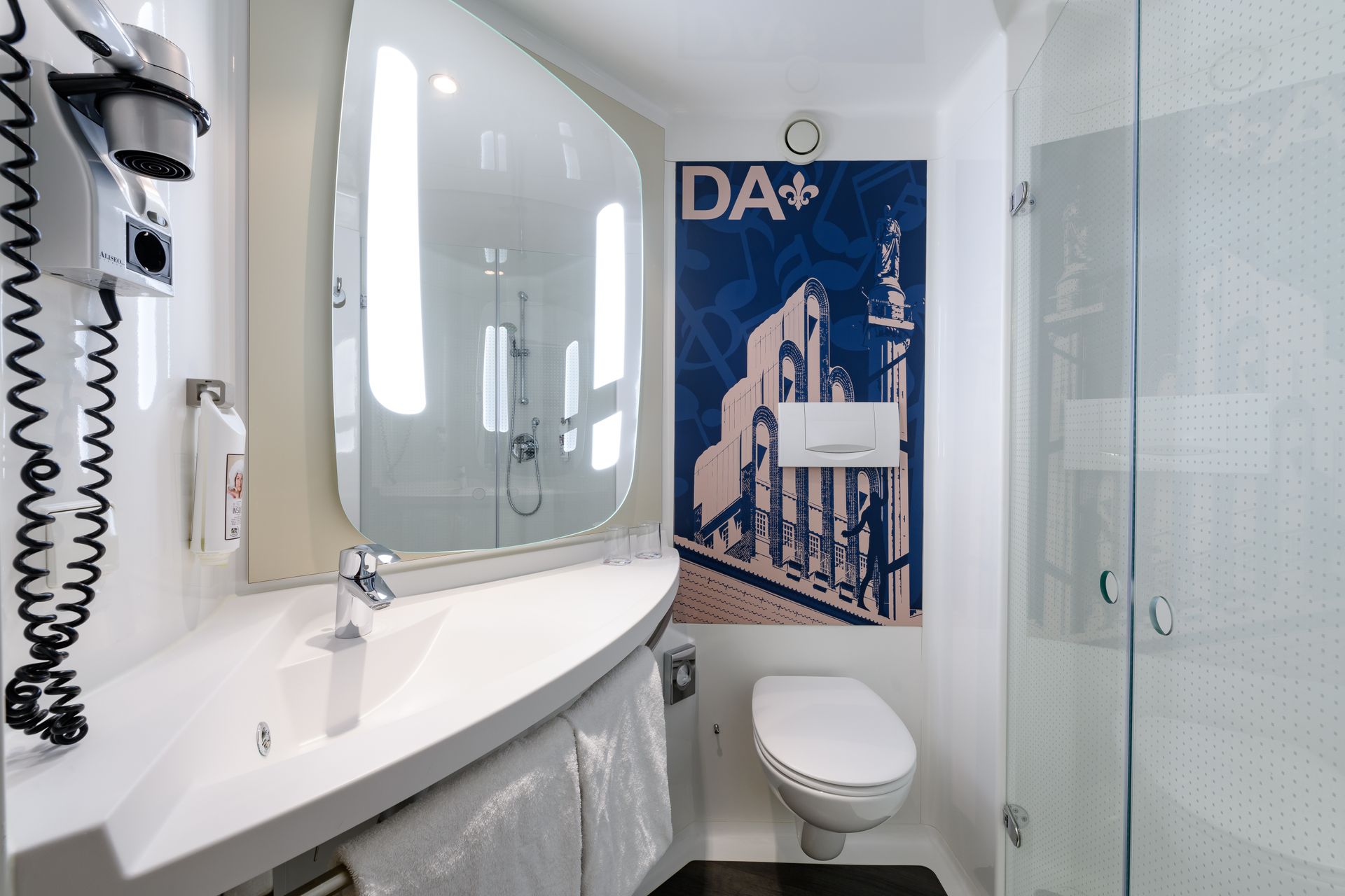 Compact white bathroom with wall-mounted sink, mirror, toilet, and blue shower curtain.