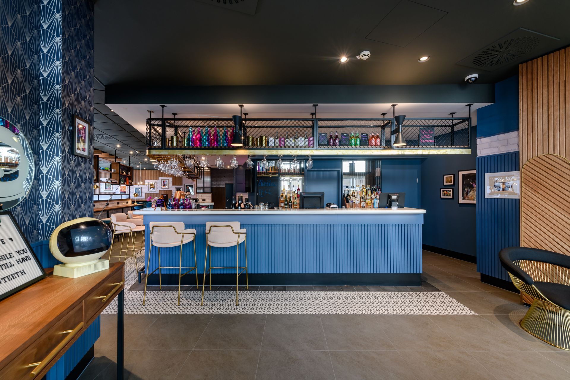 Modernes blaues Bar-Interieur mit Regalen, Barhockern und gemusterten Fliesenböden