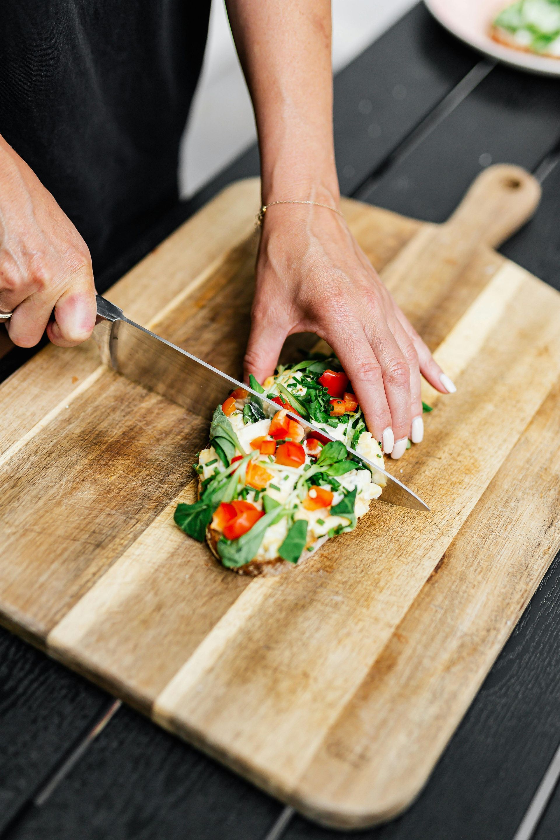 Hands slicing a vegetable-topped dish on a wooden cutting board in a kitchen