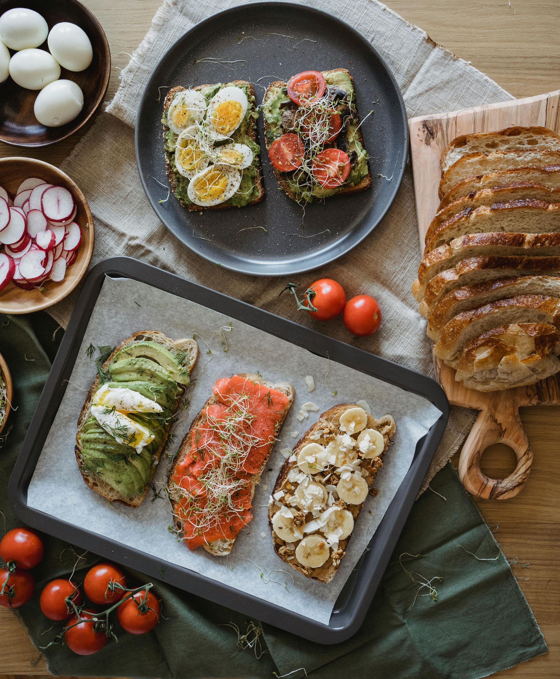 Assorted bruschetta on plates with eggs, tomatoes, radishes, and sliced bread on a rustic table.
