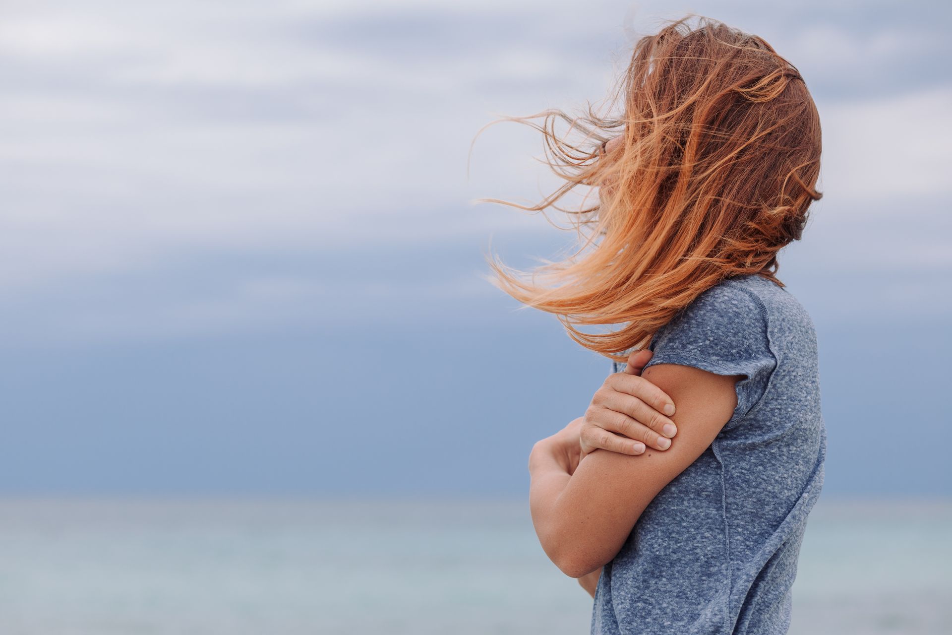 A woman is standing on the beach with her hair blowing in the wind.