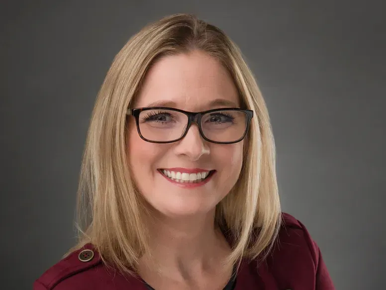 A woman wearing glasses and a red jacket is smiling for the camera.
