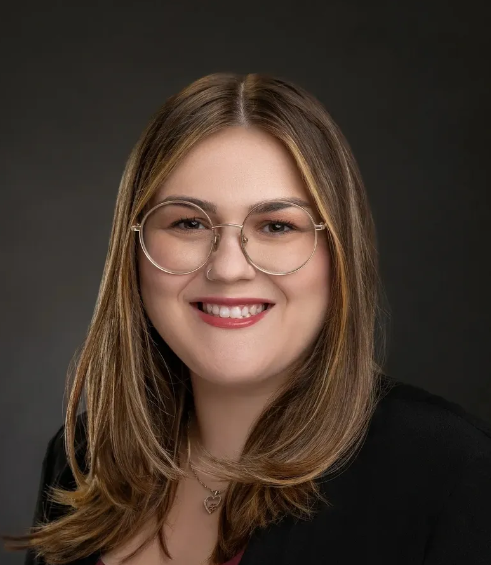 A woman wearing glasses and a black jacket smiles for the camera