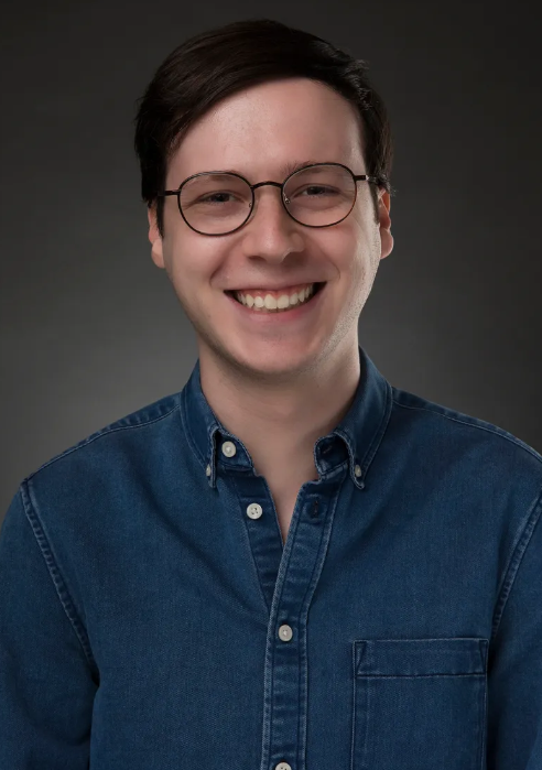 A man wearing glasses and a blue shirt smiles for the camera