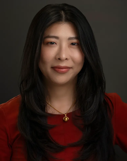 The woman is wearing a red shirt and a gold necklace.