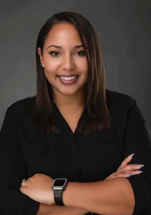 A woman wearing a black shirt and a watch is standing with her arms crossed.