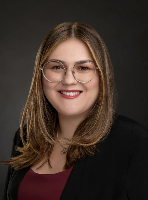 A woman wearing glasses and a black jacket is smiling for the camera.