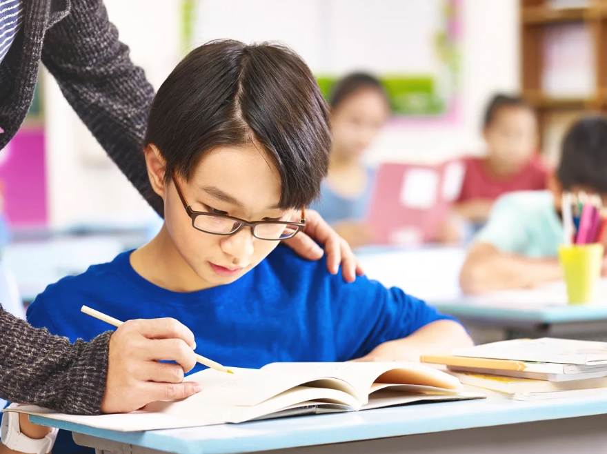 A teacher is helping a young boy with his homework in a classroom.