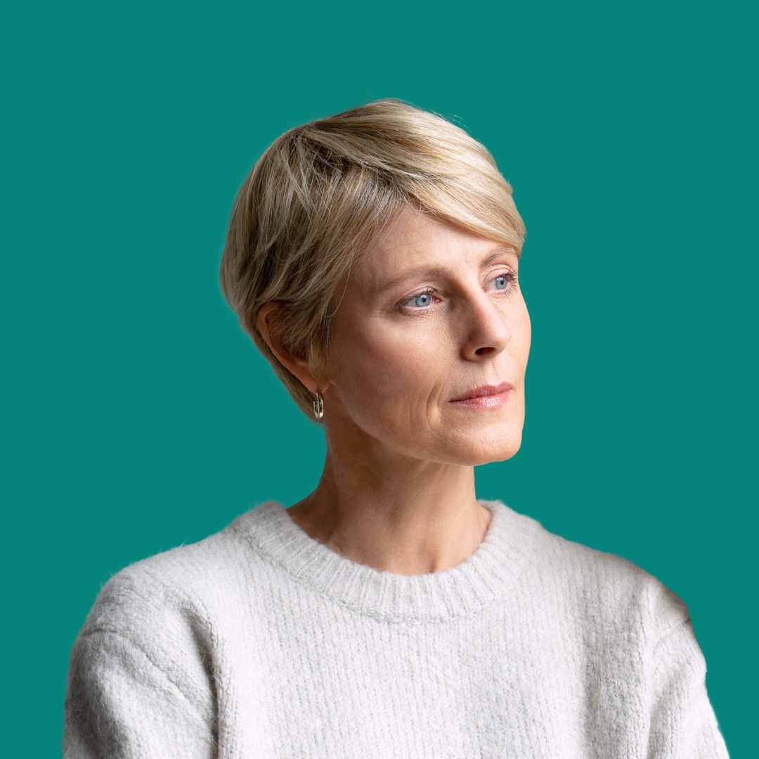 A woman wearing glasses and a white sweater is standing in front of a green background.