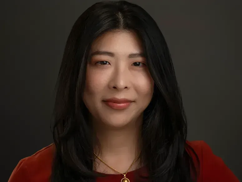 A woman with long black hair is wearing a red shirt and a gold necklace.