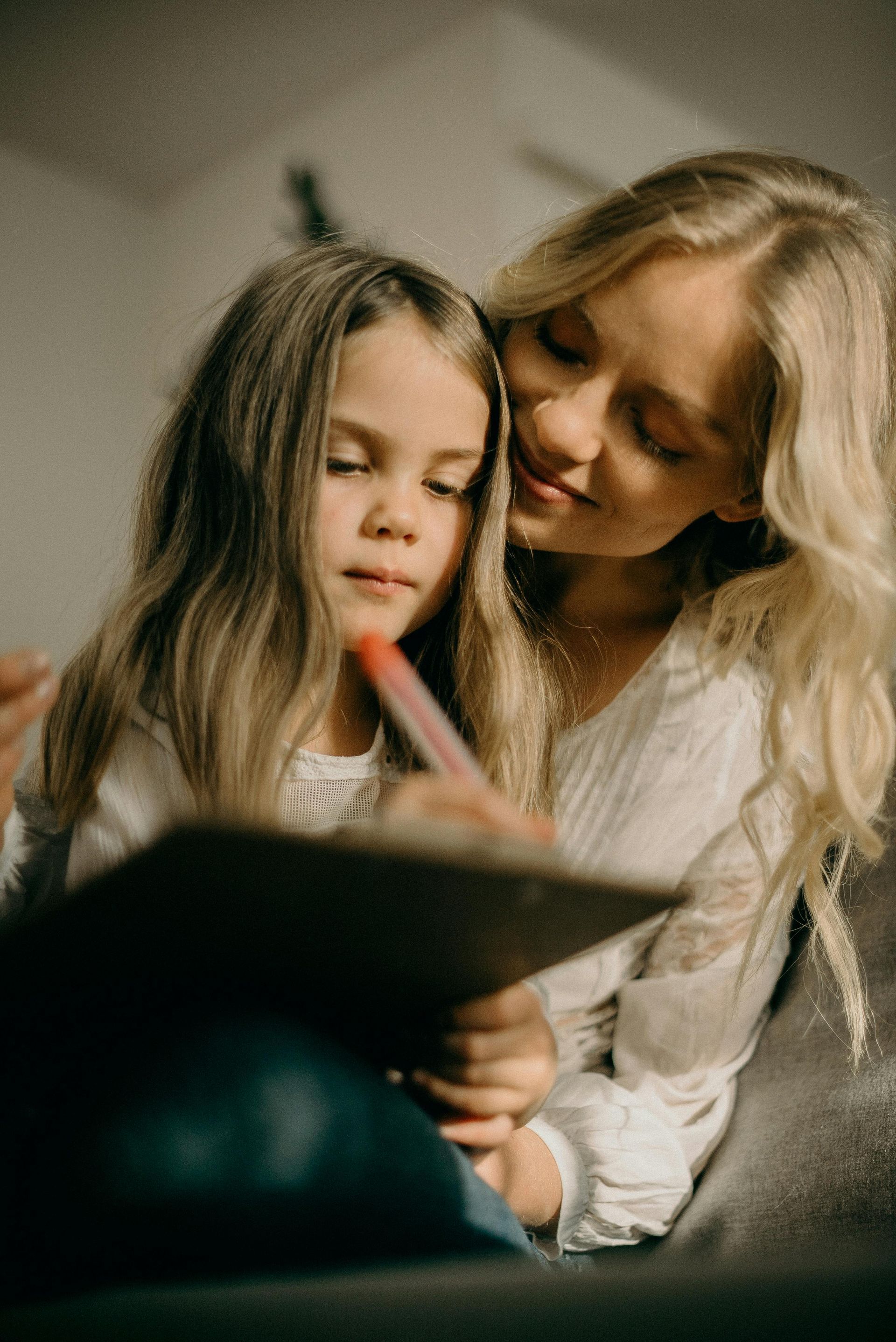 A woman and a little girl are sitting on a couch reading a book together.