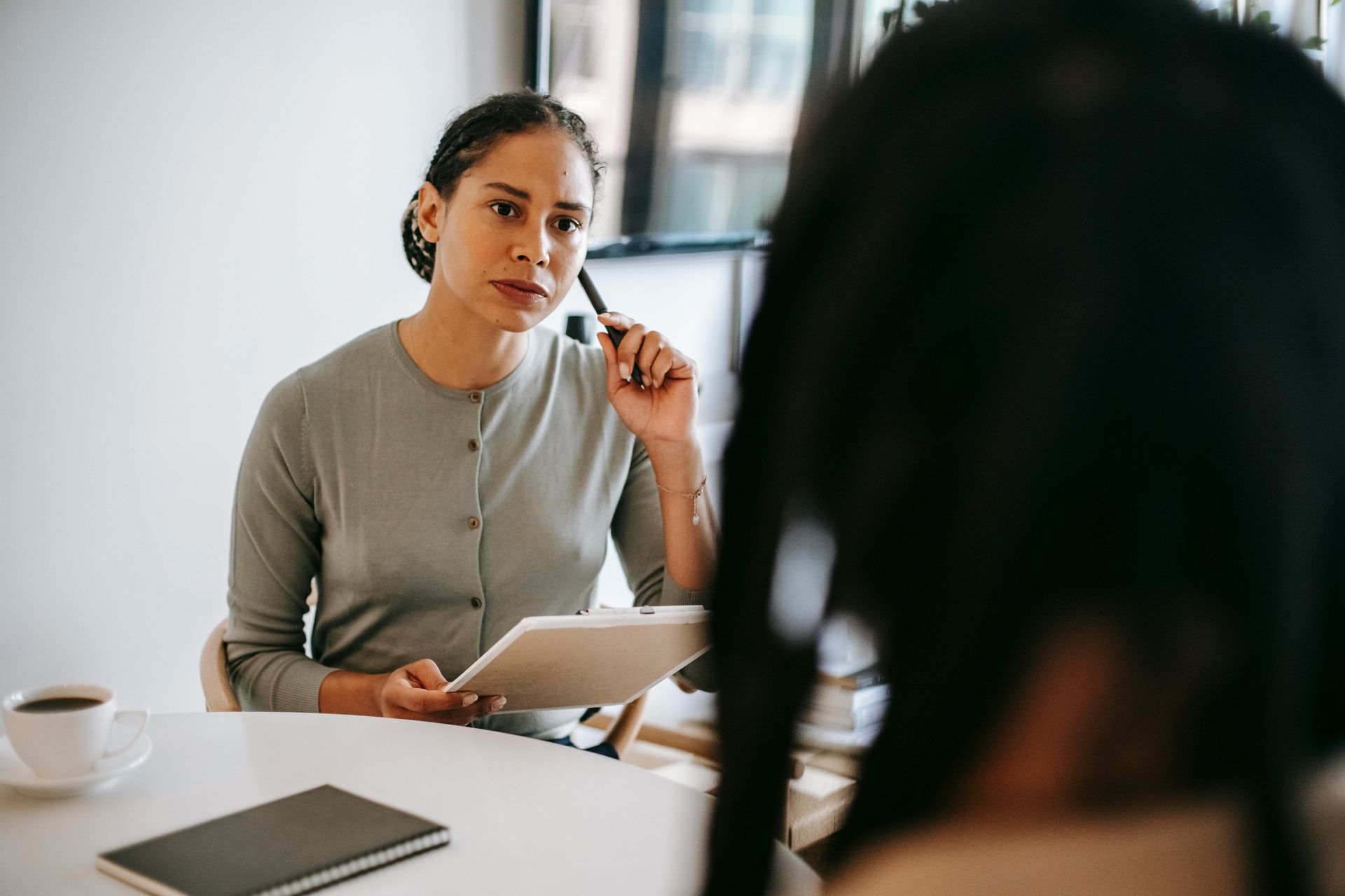 A woman is sitting at a table holding a tablet and talking to another woman.