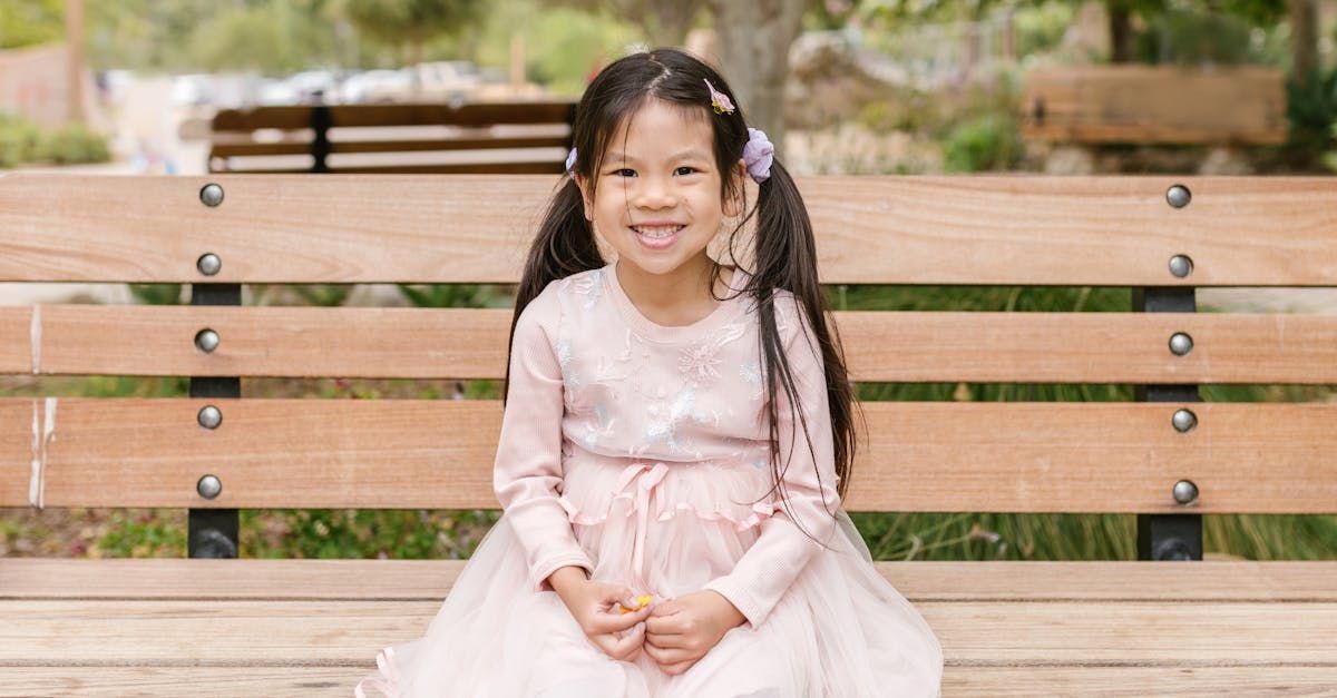 A little girl is sitting on a wooden bench in a park.