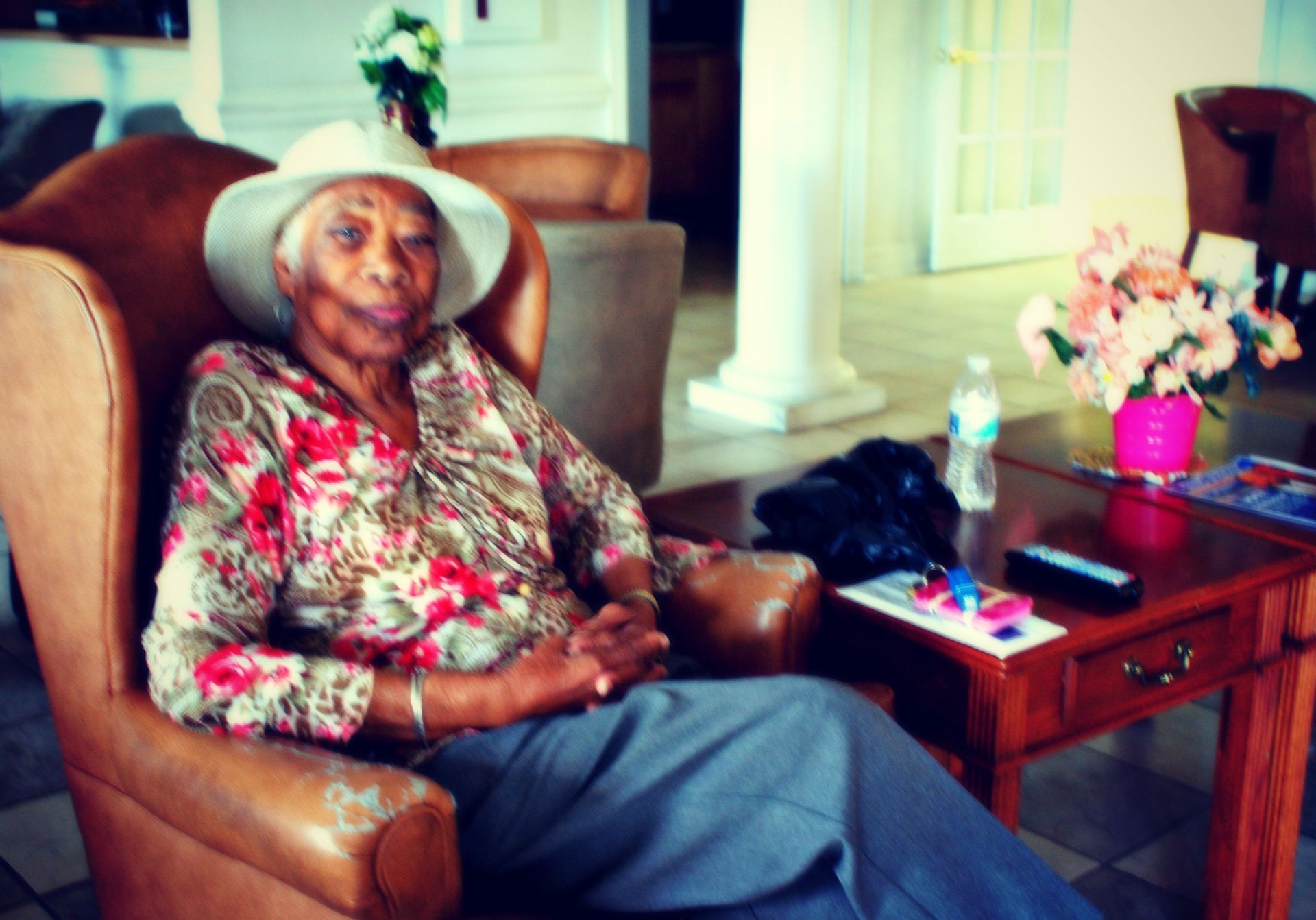 An elderly woman wearing a hat is sitting in a chair