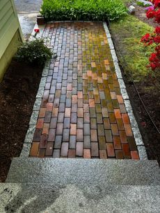 Brick walkway bordered by gravel, leading from steps up to a garden, with green plants and red flowers.