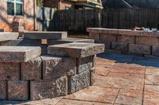 Stone fire pit and low wall on a paved patio, backyard setting.