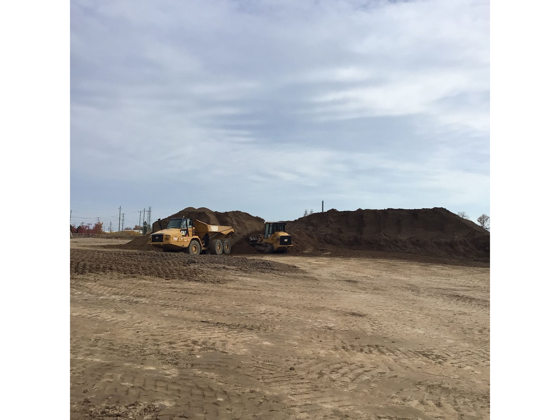 Blue-Con tractors are sitting in a dirt field next to a pile of dirt.