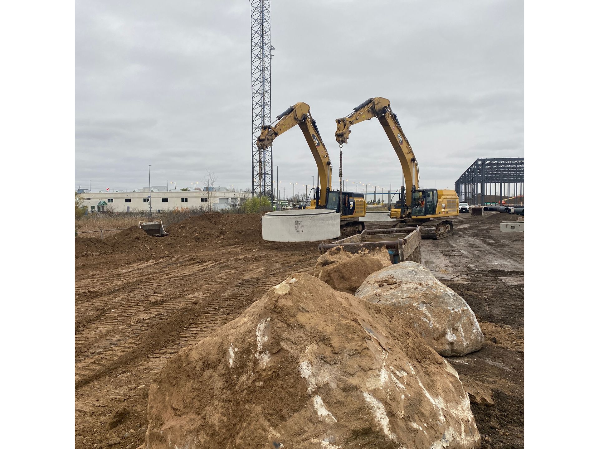 Two excavators are working on a construction site next to a pile of dirt.