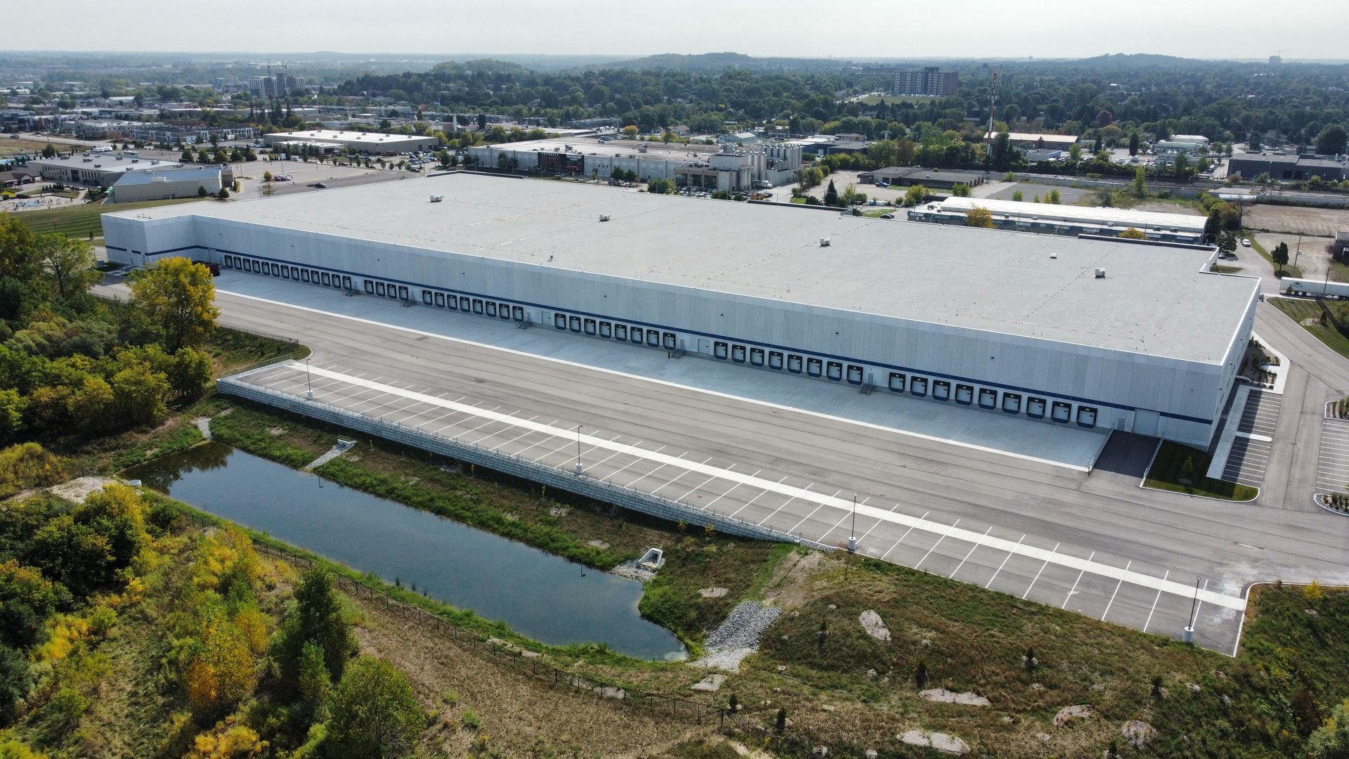 An aerial view of a large warehouse with a pond in front of it.
