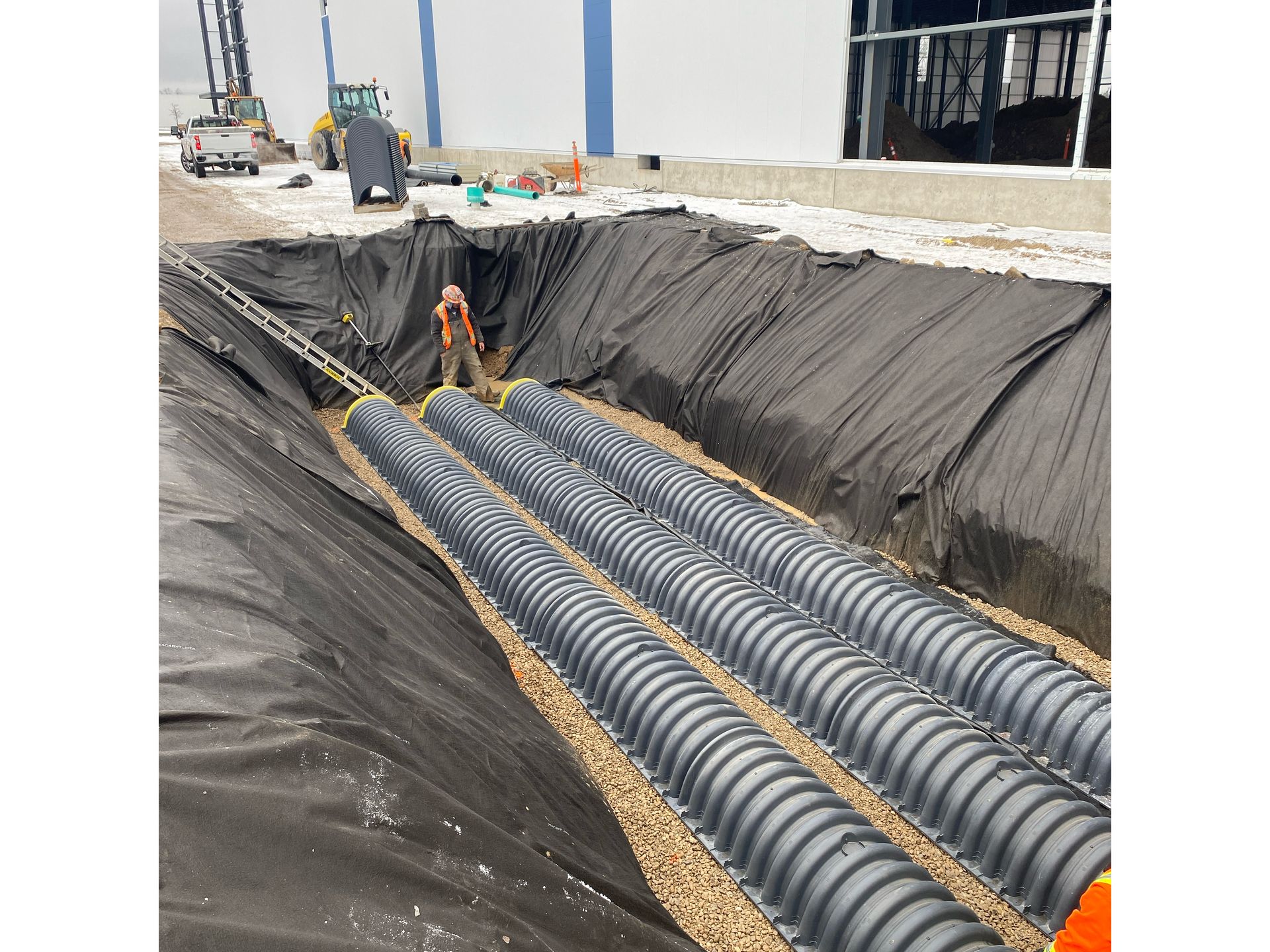 A man is standing in a trench with a bunch of pipes in it.