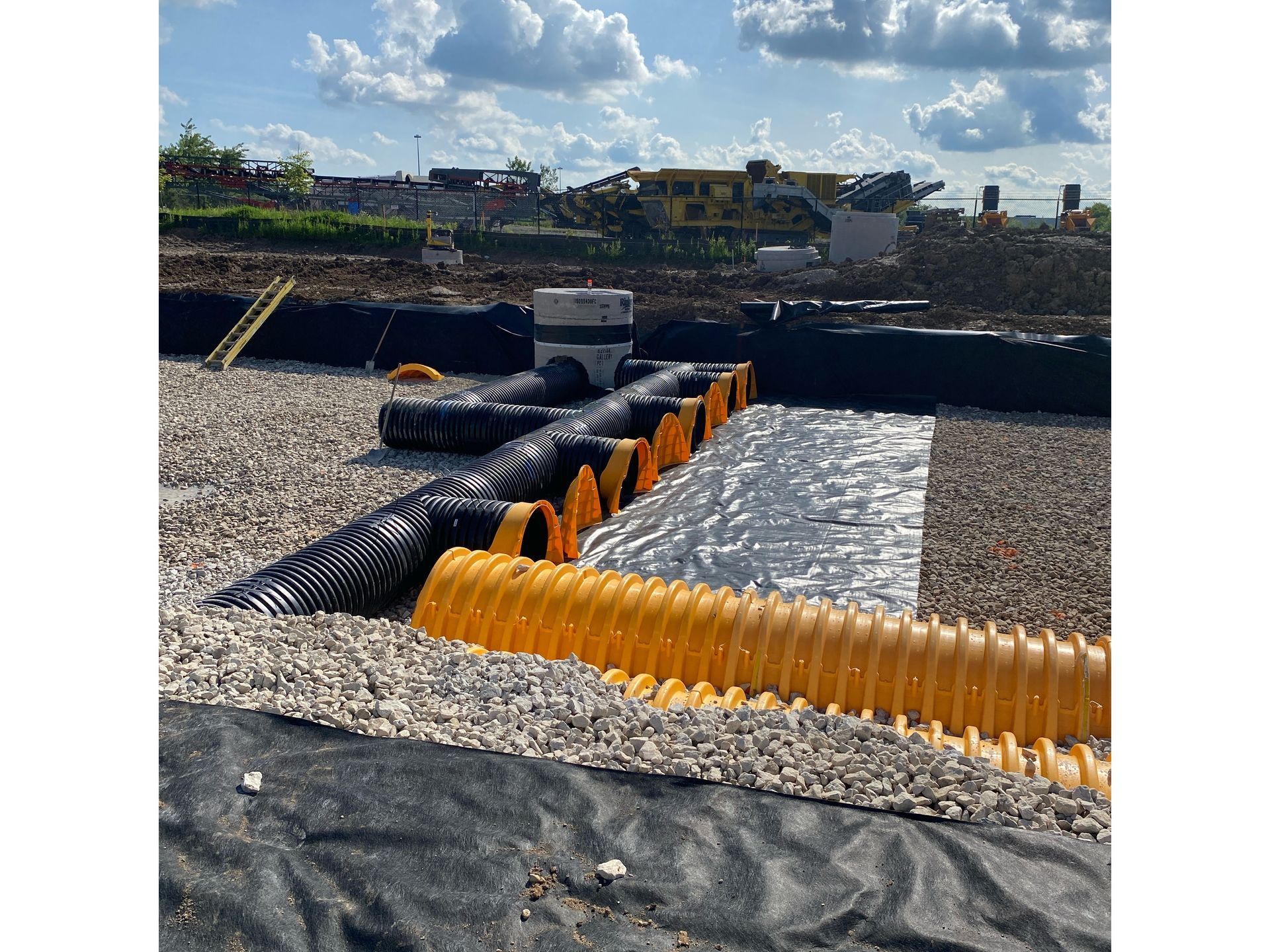 Site Servicing yellow pipes are sitting on top of a gravel road