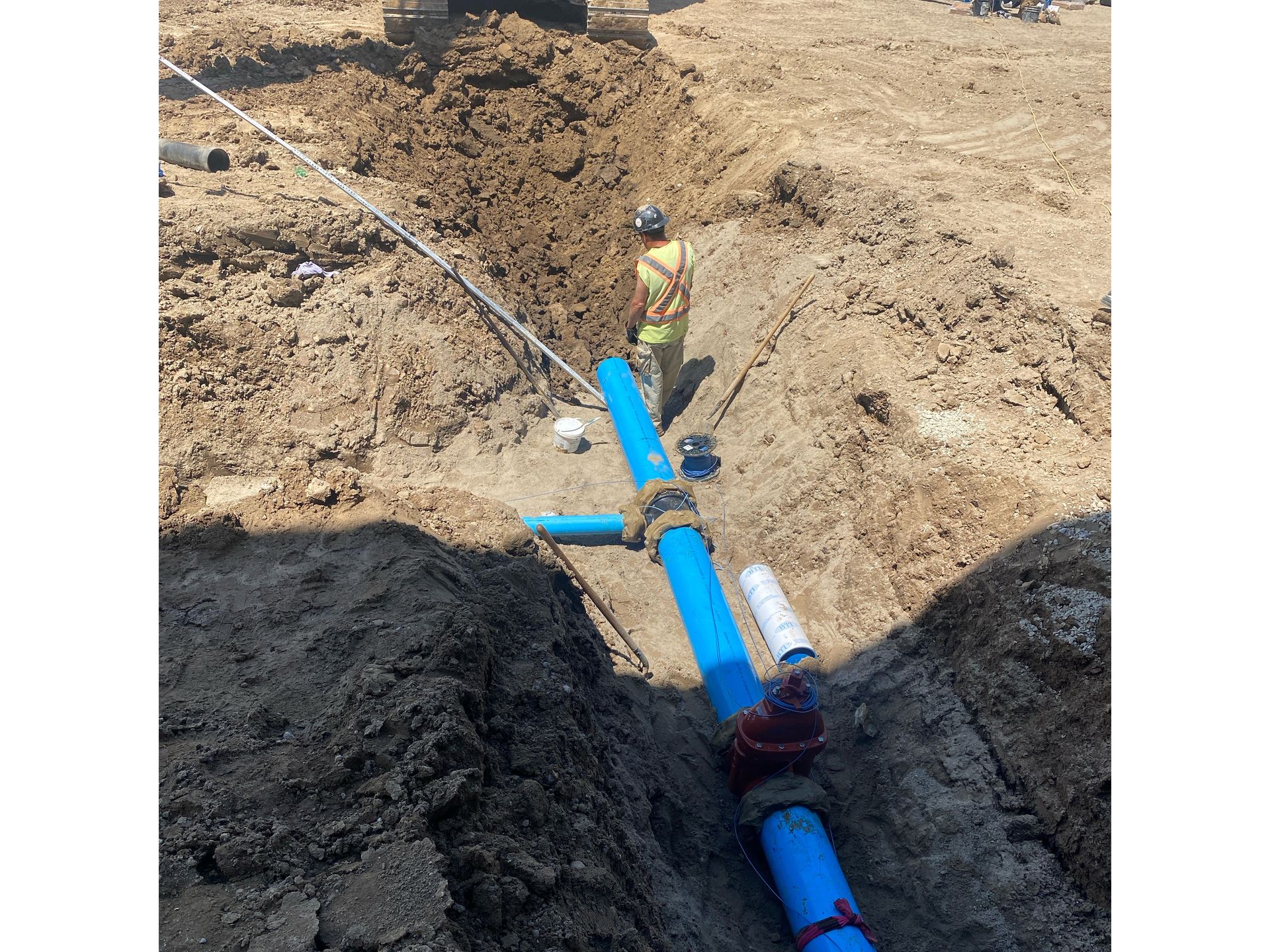 A man is standing in the dirt next to a blue pipe.