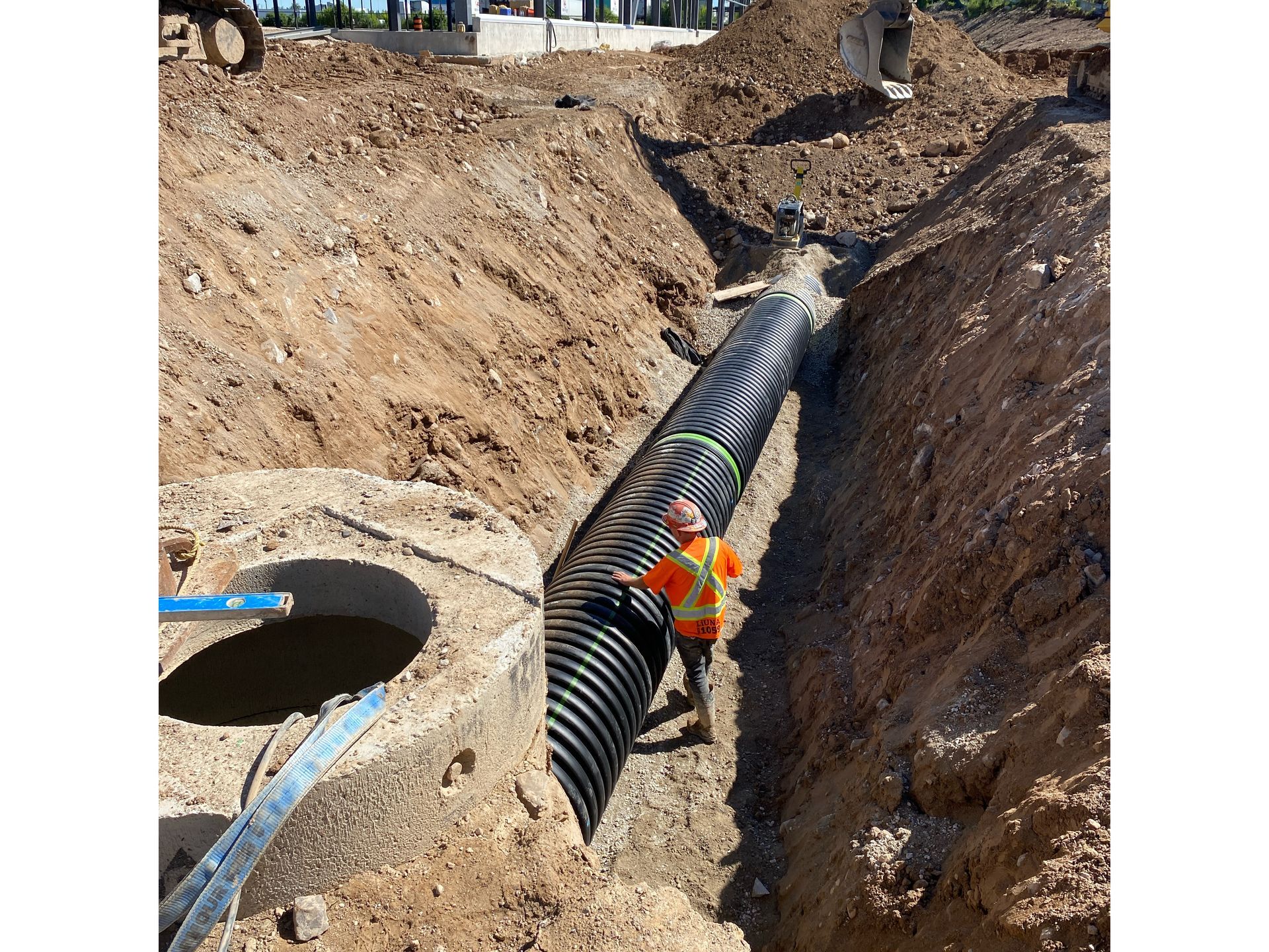 A man is standing in a trench next to a large pipe.