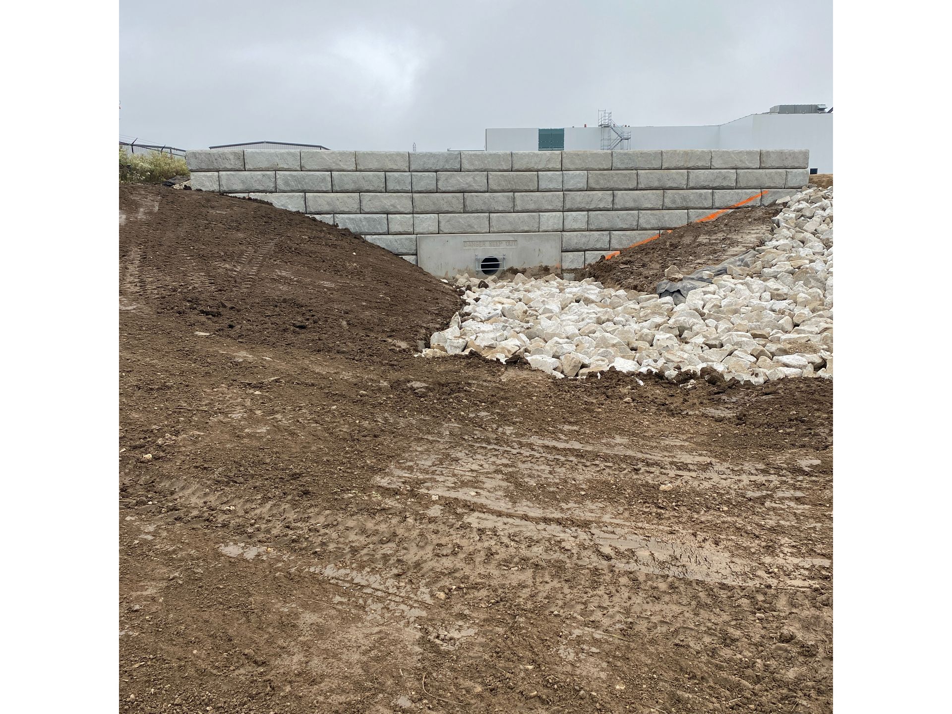 A pile of dirt and rocks in a field with a brick wall in the background.