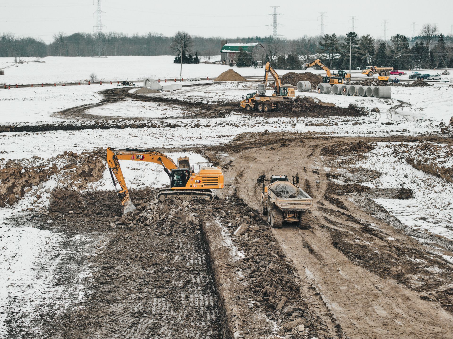 A group of construction vehicles are working on a dirt road in the snow  in St. Thomas