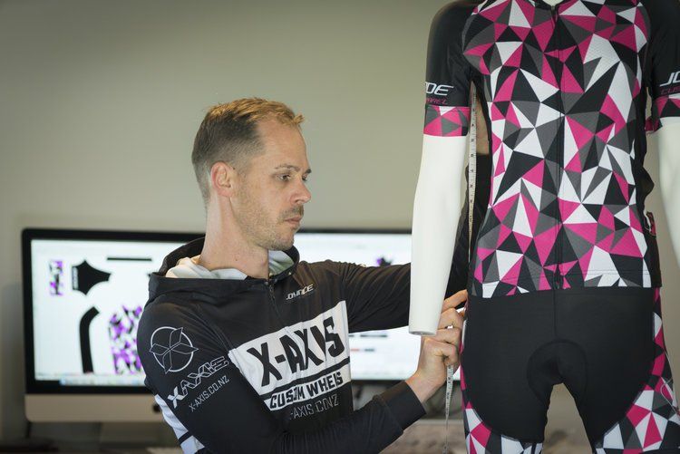 Joyride Cycling Apparel | A man is kneeling down in front of a mannequin wearing a pink and black shirt.