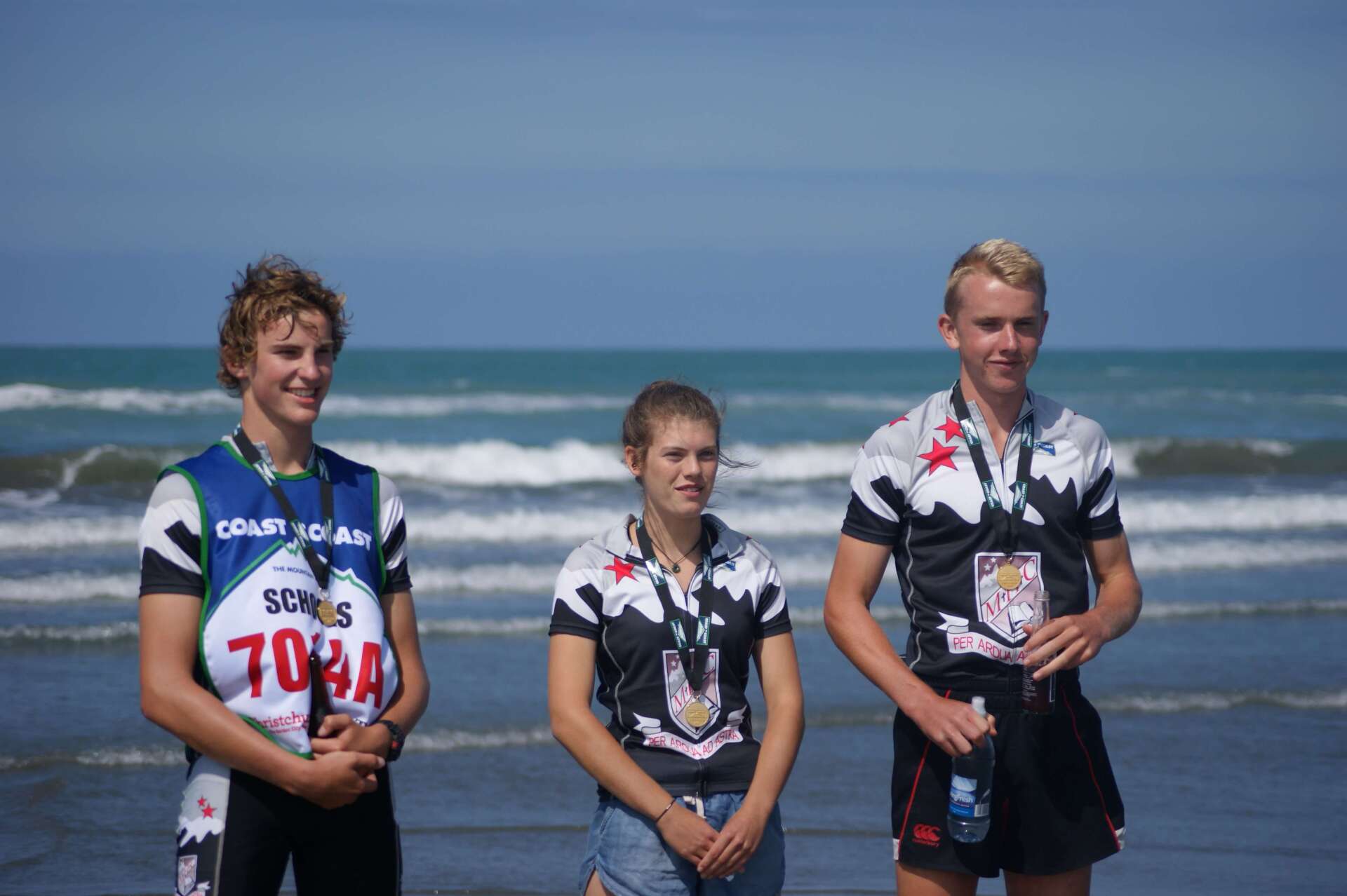 Three people are standing on a beach with medals around their necks.