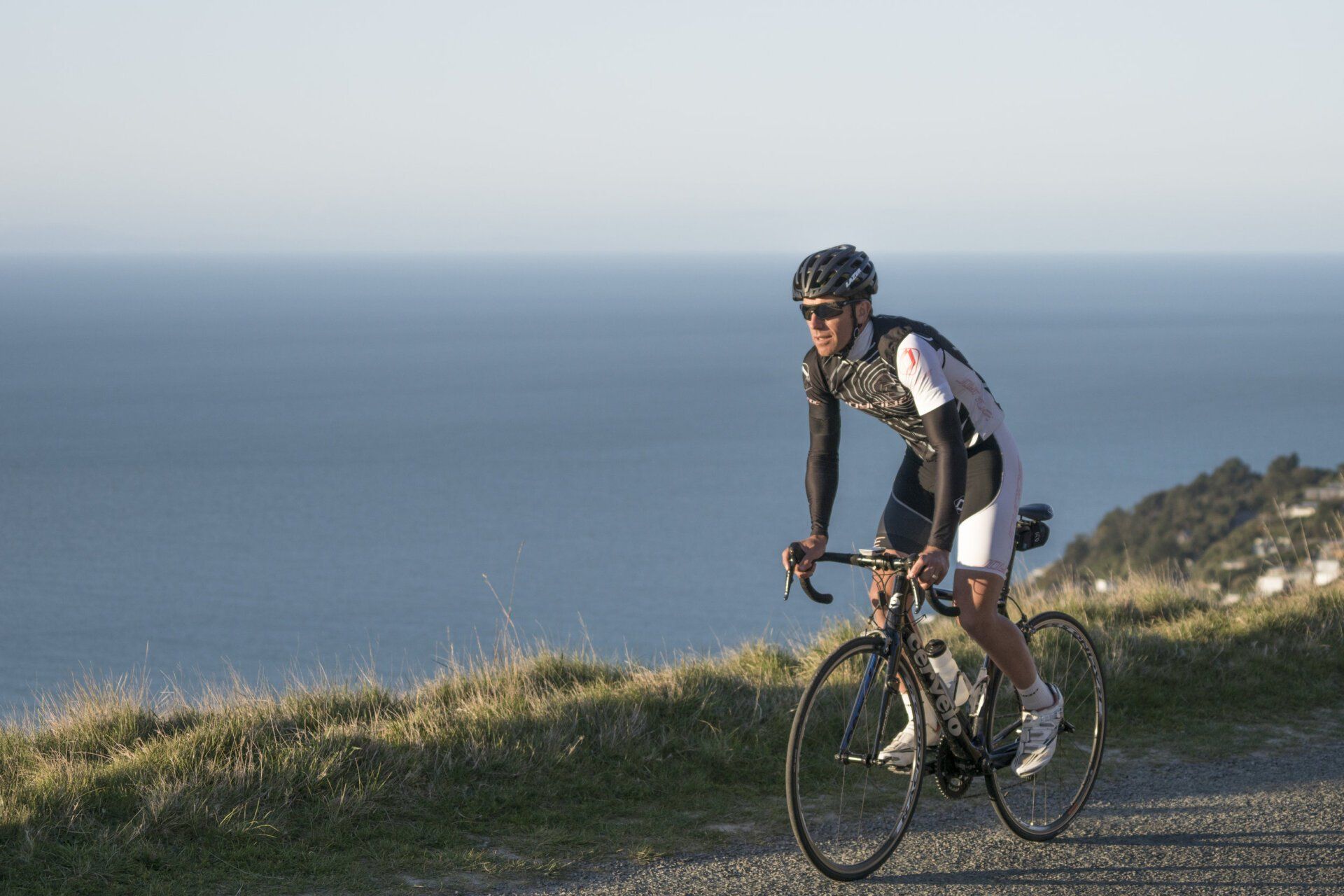 Joyride Cycling Apparel | A man is riding a bike on a dirt road near the ocean.