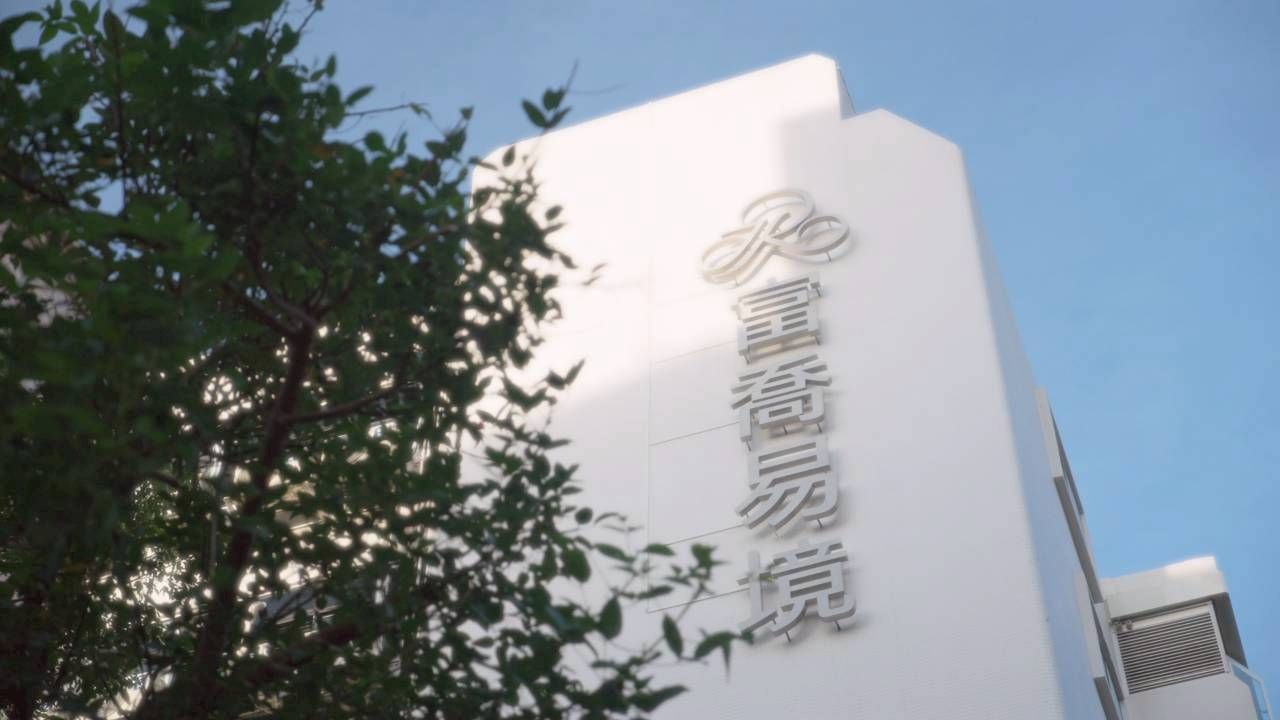 A tall white building under a clear blue sky, featuring a prominent vertical sign with Chinese characters and a tree.