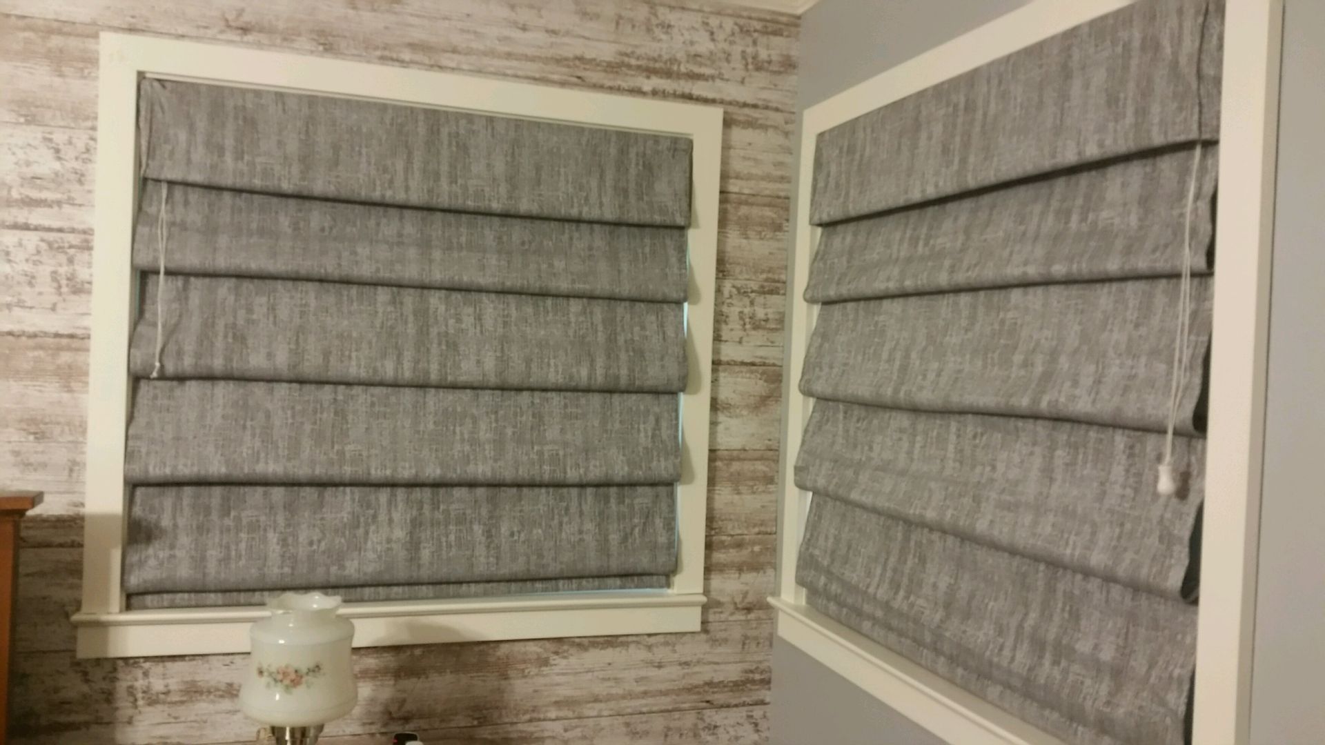 Two gray roman shades are hanging on a window in a bedroom  — East Peoria, IL — Blinds For Less