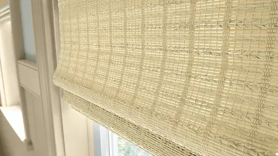 A close up of a wicker roman shade on a window.