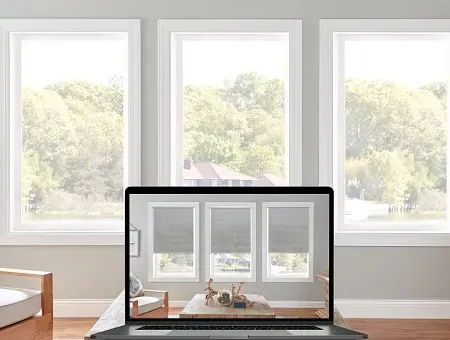 A laptop computer is displaying a living room with three windows and blinds.