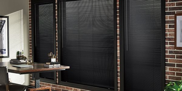 A room with a brick wall and black blinds on the windows.