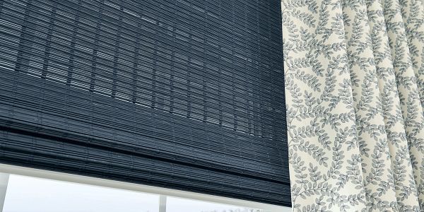 A blue roman shade is hanging on a window next to a white curtain.